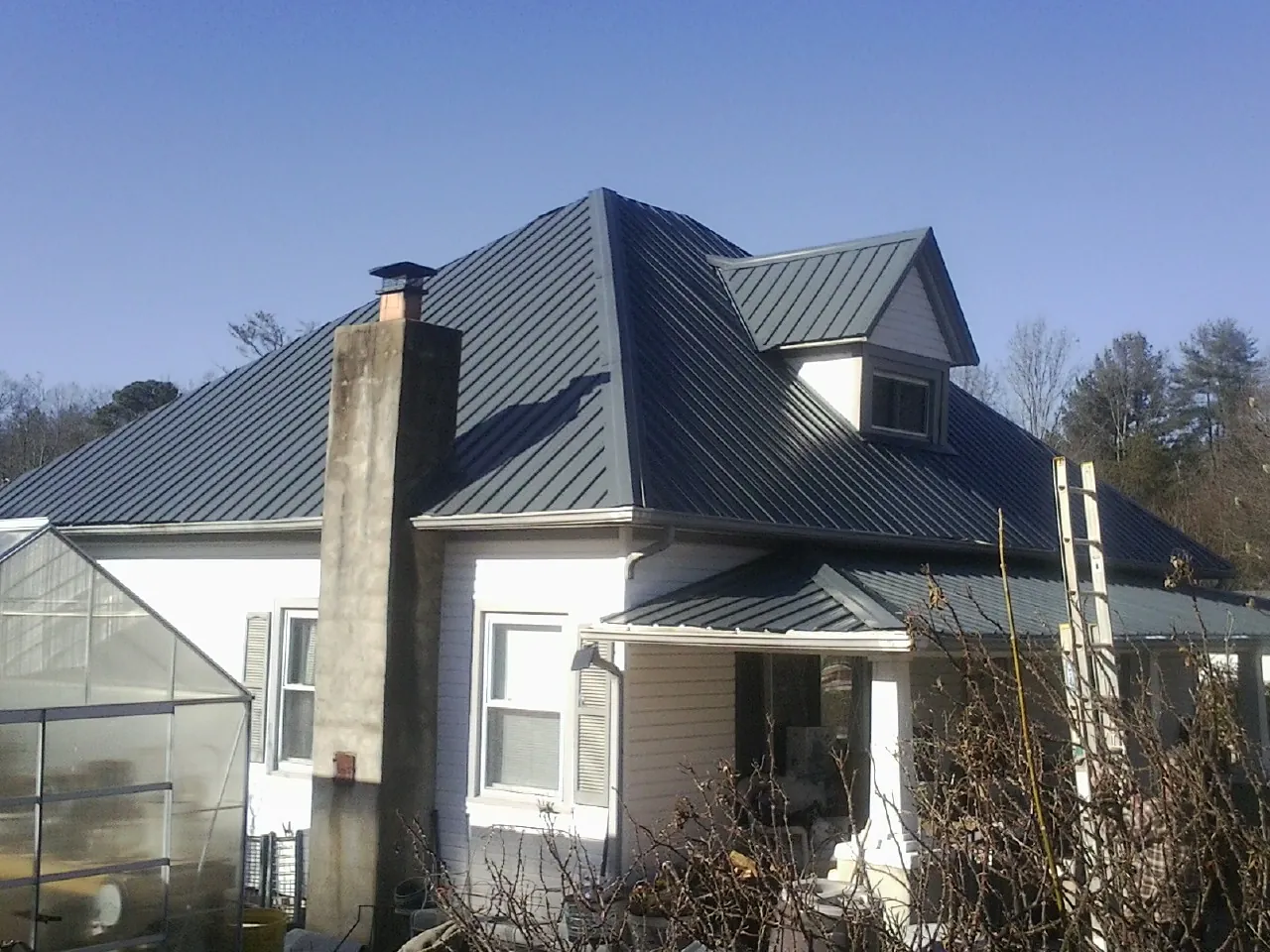 Dark blue standing seam metal roof on a white farmhouse with dormer — Slate & Tile Roof Repair by Roofing Brothers in Orchard Park