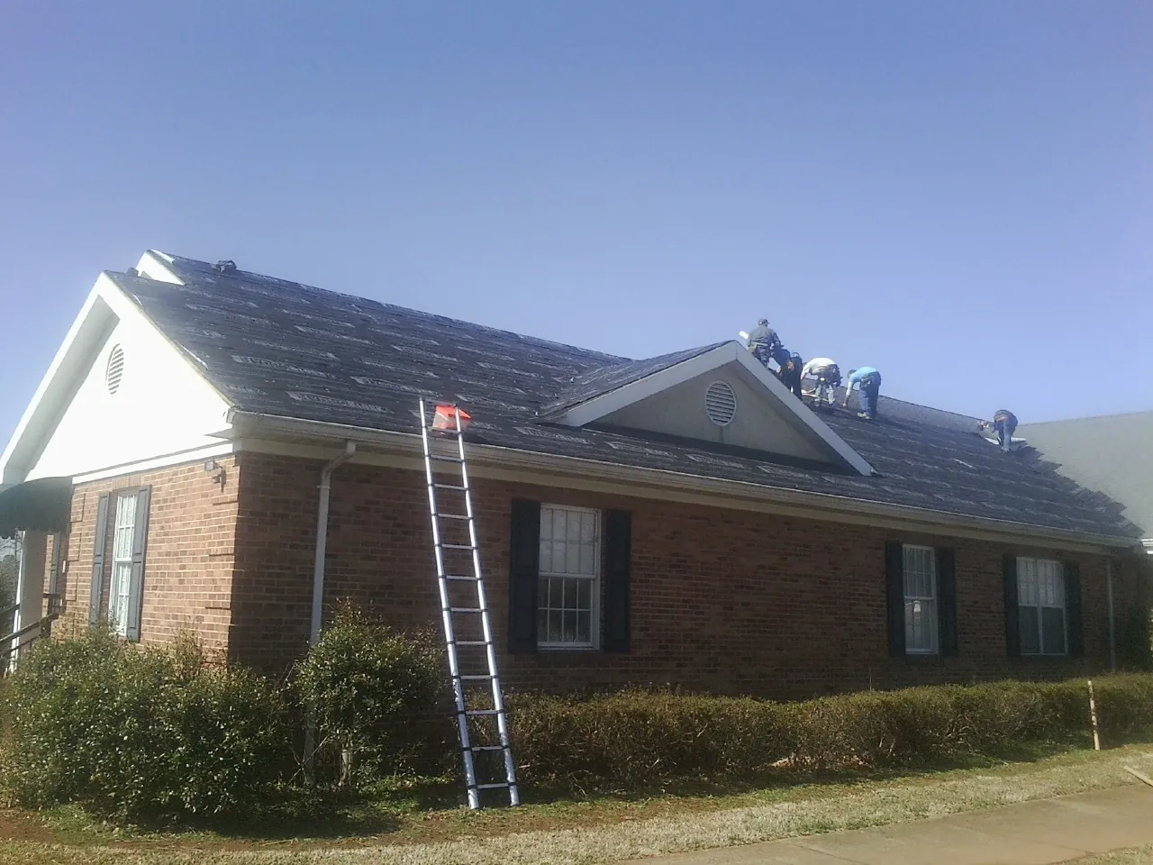 Crew tearing shingles off a brick ranch roof with a ladder set — Emergency Roof Repair work by our crew in Orchard Park