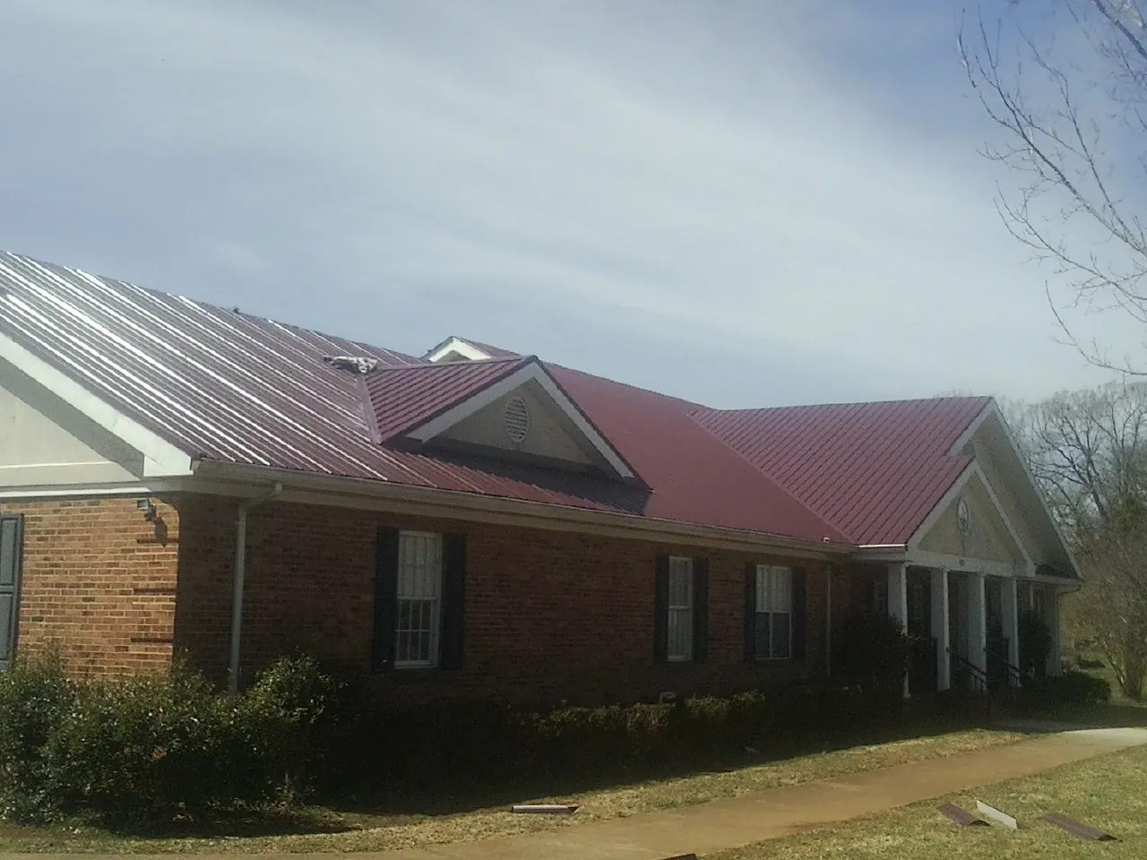 Red metal roof with gabled entries on a long brick building, from a Hail Damage Roof Repair job in Orchard Park