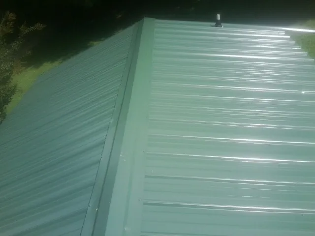 New green metal panels meeting at the ridge of a roof — Flat Roof Repair work by our crew in Orchard Park