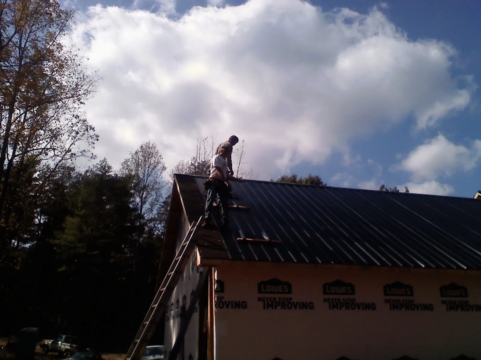 Roofer fastening dark metal panels high against a cloudy sky, from a Roof Inspection job in Orchard Park