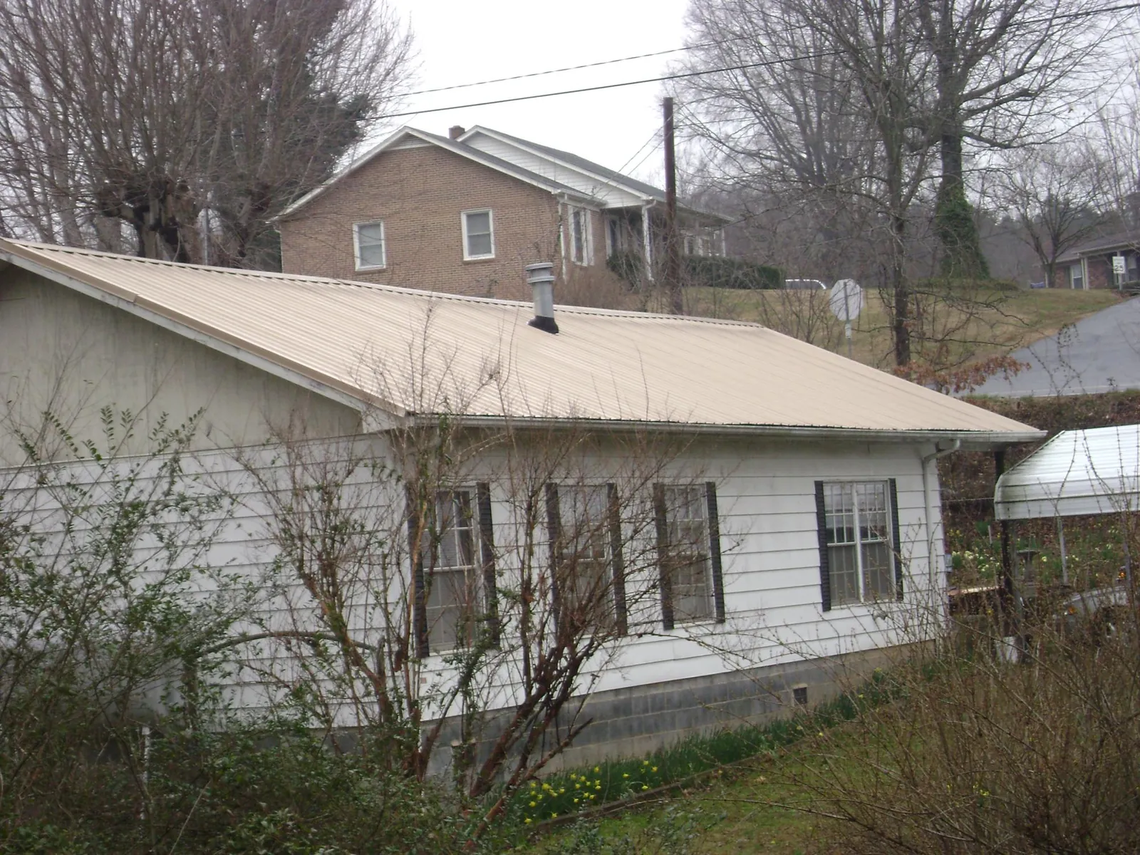 Tan metal roof on a white sided house set into a hillside — Commercial Roofing by Roofing Brothers in Orchard Park